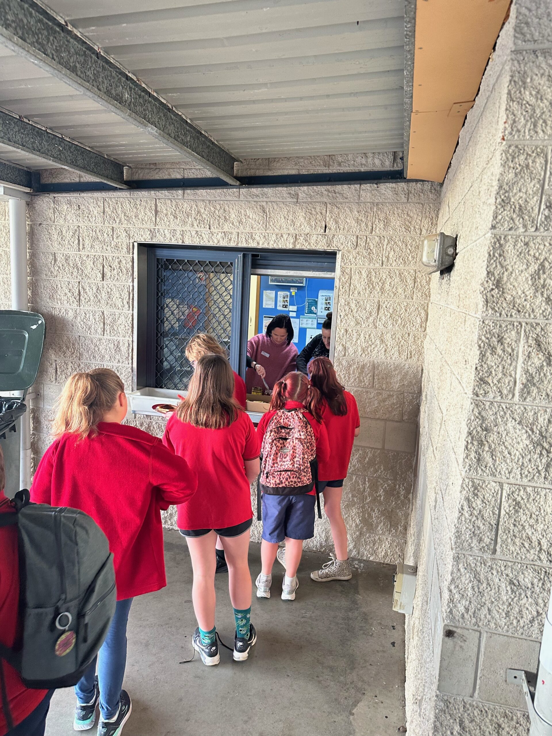 children in red uniforms lining up to a window serving breakfast